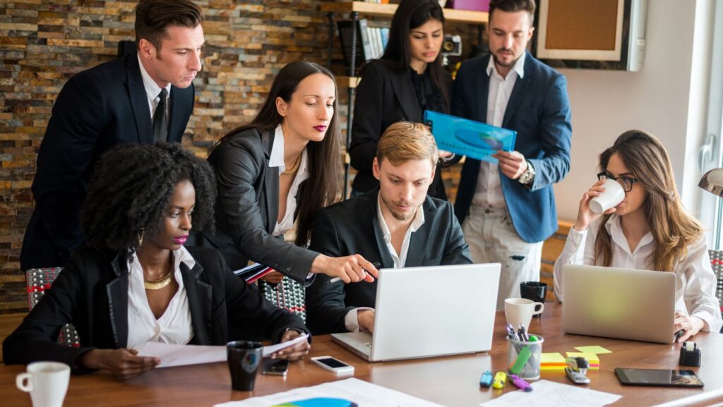 Team members standing around a table in an office, engaged in a discussion about Kanban inventory systems.